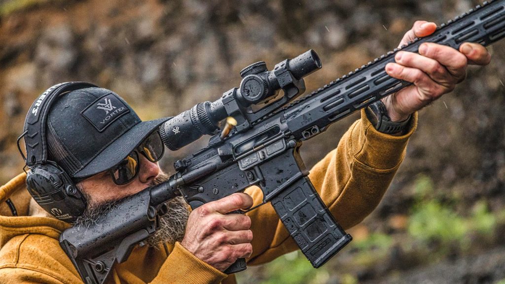 A shooter aiming a semi-automatic rifle fitted with a low-power variable optic
