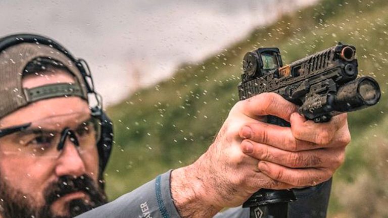 A shooter firing a pistol fitted with an enclosed-emitter red dot sight and a weapon light