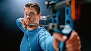 Archer at full draw with a blue compound bow, aiming towards the camera
