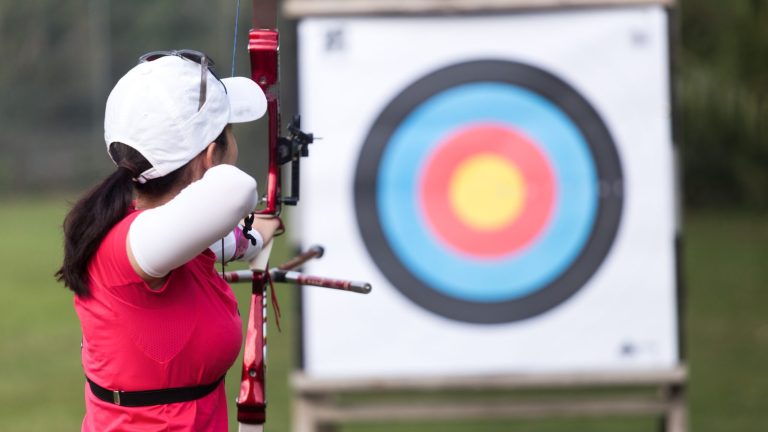 Target archer at full draw with a recurve bow beside a target boss