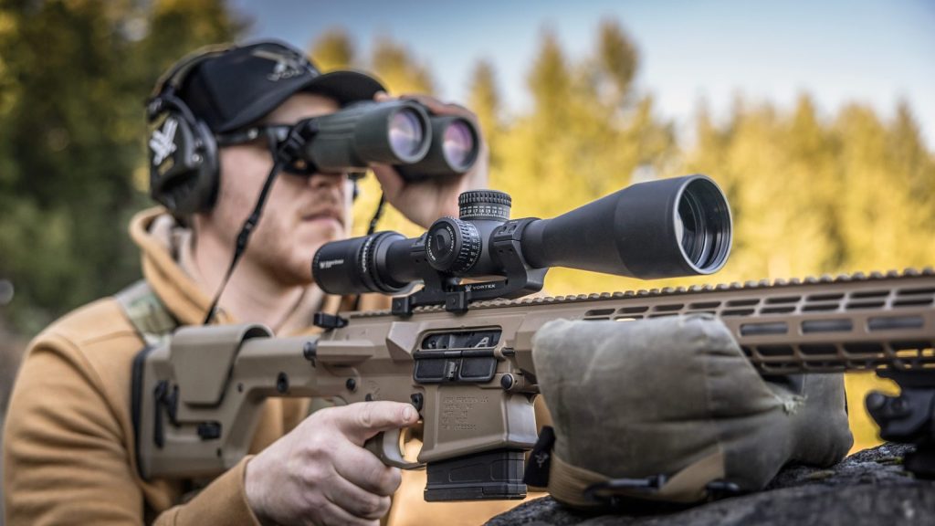 Shooter glassing with binoculars behind a precision rifle with its riflescope on a Vortex Pro Cantilever Mount